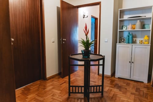 Cascais Garden House entryway with herringbone wood floors, black side table with red plant, and white storage cabinet