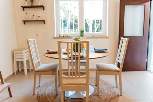 Modern dining area in Cascais Garden House with wooden round table, light chairs, and garden views through windows