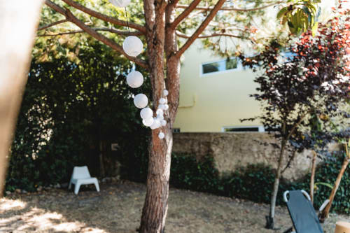 Cascais garden courtyard with white hanging lanterns, mature tree, lounger, and ivy-covered walls at Arestas e Planetas.