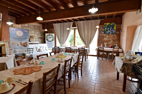 Sala da pranzo rustica presso l'agriturismo Corte delle Giuggiole nel Veneto con travi in legno, tavoli apparecchiati e vista sul giardino