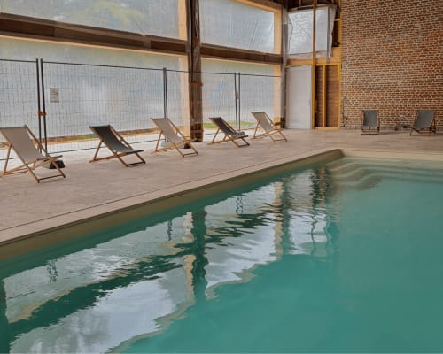 Piscine intérieure du Domaine Les Racines B&B à Croix-Moligneaux avec transats et murs en brique