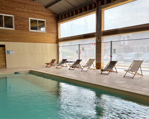 Piscine intérieure du Domaine Les Racines avec transats et grandes baies vitrées donnant sur Croix-Moligneaux
