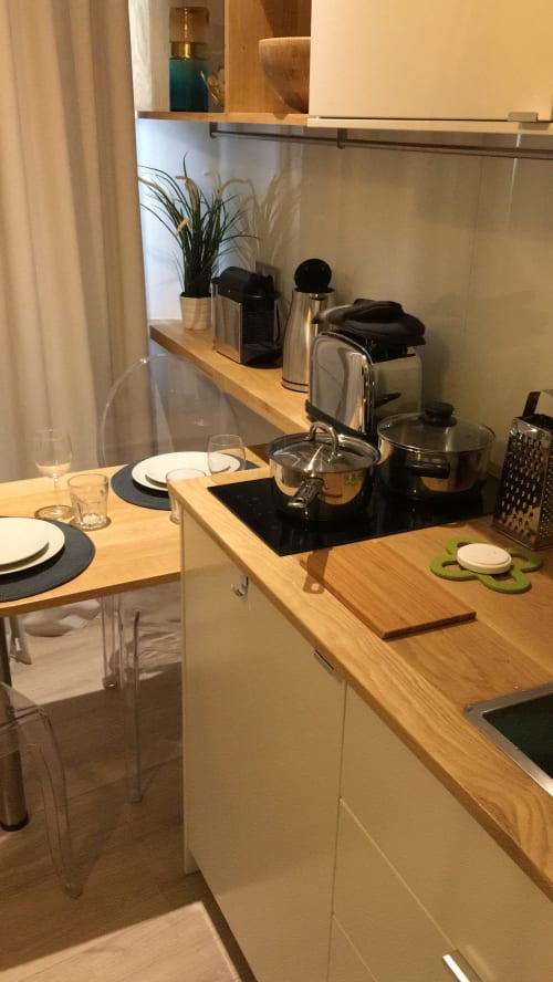 Modern kitchenette in Cocoon Gallery Paris studio with wooden counter, stovetop, espresso machine, and dining area with place
