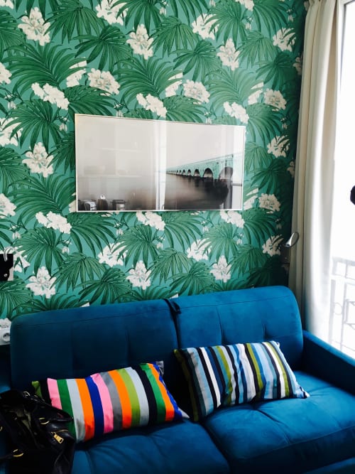 Blue velvet sofa with striped cushions against tropical leaf wallpaper in Cocoon Gallery Paris studio room