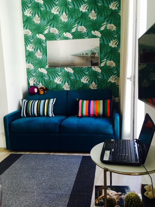 Modern studio at Cocoon Gallery Paris with blue sofa, tropical wallpaper, striped pillows, and flat-screen TV above seating