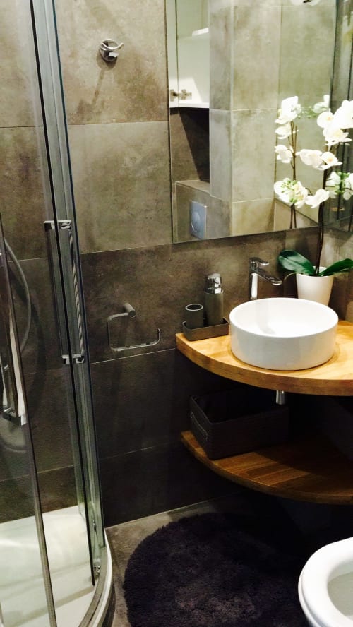 Modern bathroom at Cocoon Gallery Paris with vessel sink, dark tile walls, and glass shower enclosure with white orchids