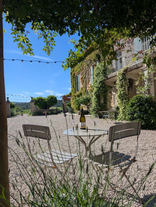 Ivy-covered stone building at Domaine de Pelican with outdoor seating and wine bottle in Gignac, France