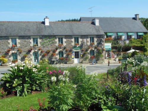 Hôtel De La Vallée à Saint-Gilles-Vieux-Marché avec façade en pierre, fleurs colorées et jardins paysagés sous ciel bleu
