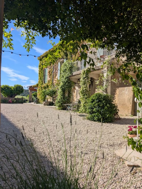 Ivy-covered stone building at Domaine de Pelican in Gignac, France, with gravel courtyard and lush green gardens under blue
