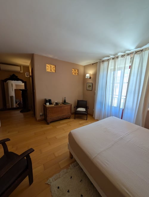 Chambre spacieuse au Domaine de Pelican avec parquet, lit blanc, mobilier vintage et baies vitrées vue jardin