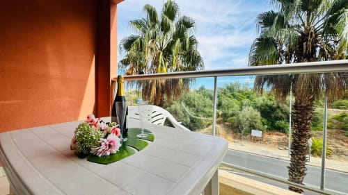 Varanda com flores rosas, cadeira branca e vista para as palmeiras do apartamento Sweet Home em Portimão, Portugal