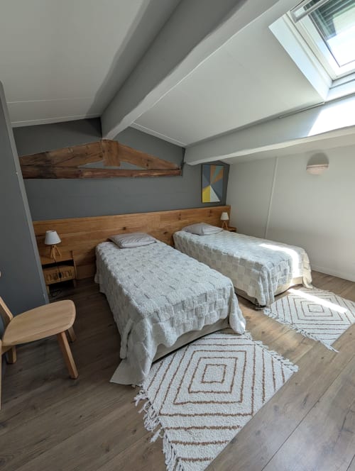 Cozy twin bedroom at Domaine de Pelican with exposed beams, wooden headboard, and geometric rugs in Gignac