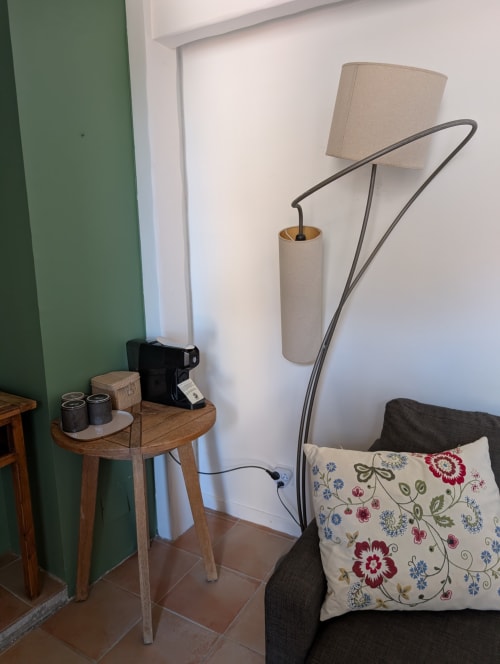 Coin de chambre d'hôtel avec lampadaire arc, canapé rembourré orné d'un coussin floral, table basse en bois et décor épuré