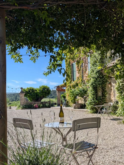 Terrasse extérieure du Domaine de Pélican avec bouteille de vin, verres et bâtiment en pierre couvert de lierre à Gignac