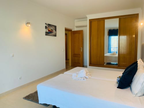 Quarto luminoso e moderno no apartamento Sweet Home Ferragudo com cama queen, guarda-roupa em madeira e vista para a cidade