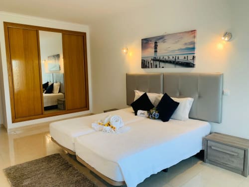 Quarto moderno do apartamento Sweet Home Ferragudo com cama king-size, cabeceira cinza, arte com farol e banheiro privativo