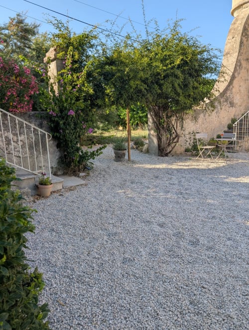 Rustic courtyard garden at Domaine de Pelican villa in Gignac with gravel patio, flowering vines, shaded trees, and outdoor