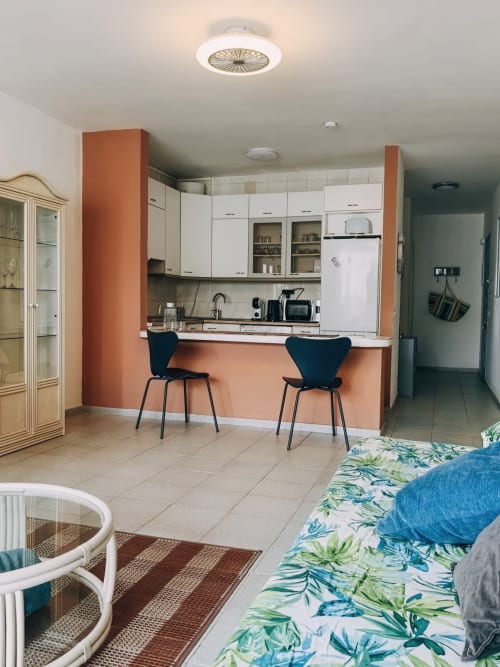 Cocina y sala de estar modernas en el apartamento Casa Ormì, Corralejo, con muebles blancos, pared acentuada en naranja y barra desayunadora