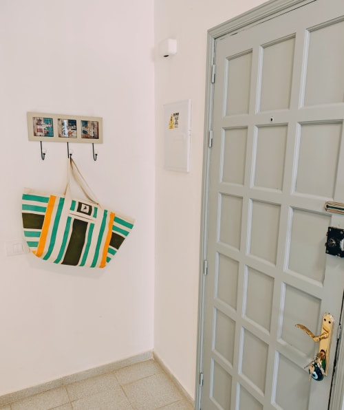 Entrada del apartamento Casa Ormì con bolsa de playa a rayas colgada en ganchos y puerta blanca panelada en Corralejo