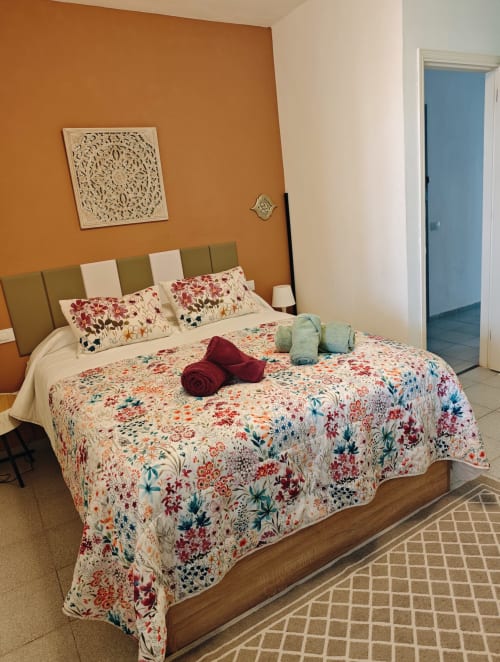 Dormitorio en Casa Ormì de Corralejo con pared de acento naranja, ropa de cama floral y cabecero tapizado