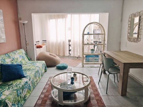 Moderno salón de apartamento en Corralejo con sofá de estampado tropical, mesa de vidrio y área de trabajo