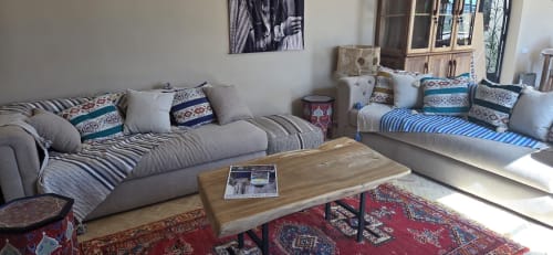 Salon du Riad Arkaya à Essaouira avec sièges gris, tissus rayés, coussins décoratifs, table en bois et rouge traditionnel