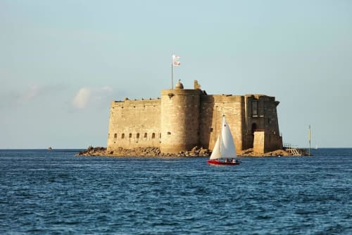 Historic stone fort with sailboat on blue water near Pleyber-Christ, France