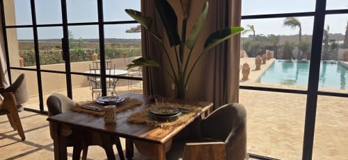 Salle à manger du Riad Arkaya avec vue sur la piscine à Essaouira. Table, chaises, plante et terrasse surplombant le domaine.