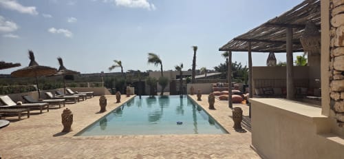 Piscine du Riad Arkaya à Essaouira avec chaises longues, palmiers et architecture traditionnelle sous ciel bleu