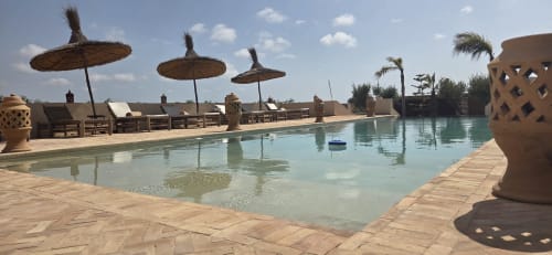 Piscine du Riad Arkaya à Essaouira : eau turquoise, parasols de chaume, transats et architecture marocaine traditionnelle