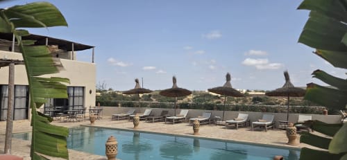 Espace piscine du Riad Arkaya à Essaouira avec chaises longues, parasols en chaume et terrasse dominant la campagne