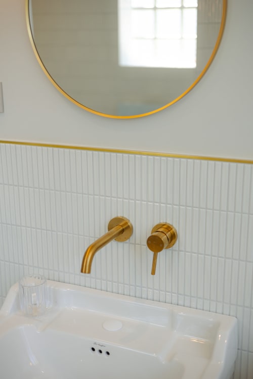 Salle de bains minimaliste à L'Ode à Pierre : carrelage blanc, robinetterie laiton, miroir circulaire et vasque blanche.
