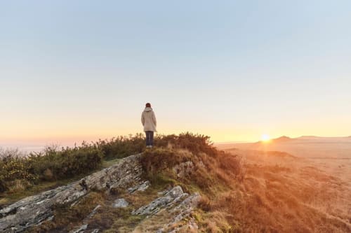 Person standing on rocky hilltop at sunset overlooking Pleyber-Christ countryside