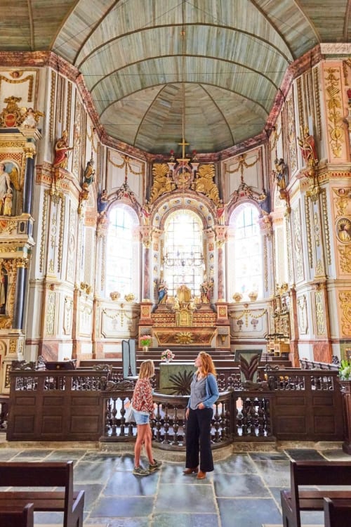 Two visitors admiring ornate Baroque chapel interior with gilded details at Gites du Bulz, Pleyber-Christ, Brittany
