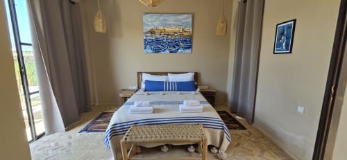 Chambre Mogador au Riad Arkaya à Essaouira : literie rayée bleue, art côtier et vue sur le jardin