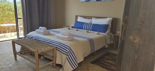 Chambre Mogador au Riad Arkaya à Essaouira : lit aux draps rayés bleus, serviettes blanches, banc en bois, portes avec vue sur jardin
