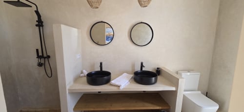 Salle de bain moderne du Riad Arkaya à Essaouira avec vasques noires doubles, miroirs ronds, douche pluie et toilettes