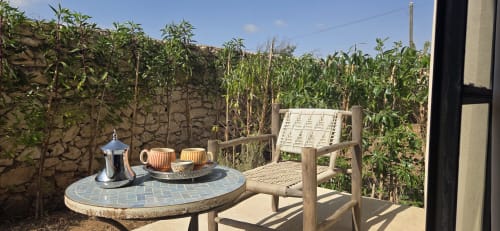 Terrasse de jardin du Riad Arkaya Essaouira avec chaise en bois, service à thé et plantes verdoyantes