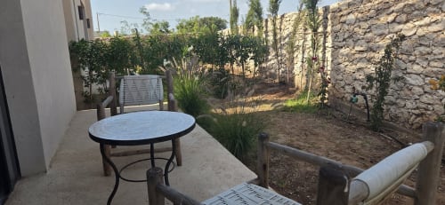 Patio du jardin du Riad Arkaya Essaouira avec table ronde, chaises longues et murs en pierre