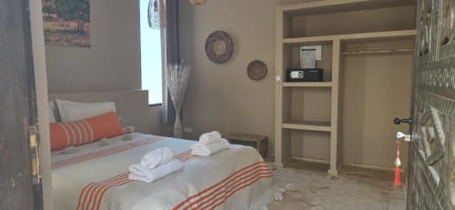 Chambre accessible au Riad Arkaya à Essaouira avec literie rayée orange, étagères et fenêtre avec vue sur la ville