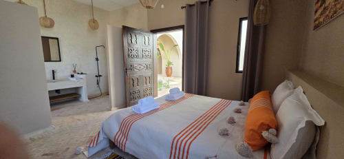 Chambre lumineuse et accessible au Riad Arkaya à Essaouira avec draps blancs, touches d'orange et salle de bain attenante