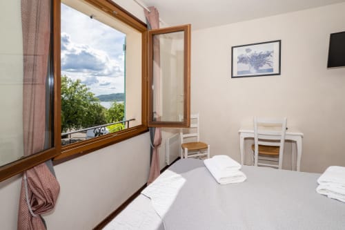 Chambre Lavande à l'Hôtel Le Verdon avec vue sur le lac depuis la fenêtre en bois, literie blanche et coin salon aménagé