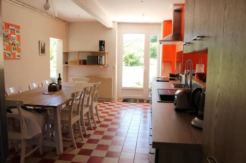 Cuisine-salle à manger lumineuse du gîte Les Petits Toits avec accents rouges, carrelage damier et vue sur le jardin