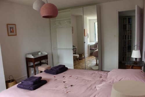 Chambre spacieuse avec literie rose au gîte Les Petits Toits à Vérac, France, armoire miroir et luminaire suspendu