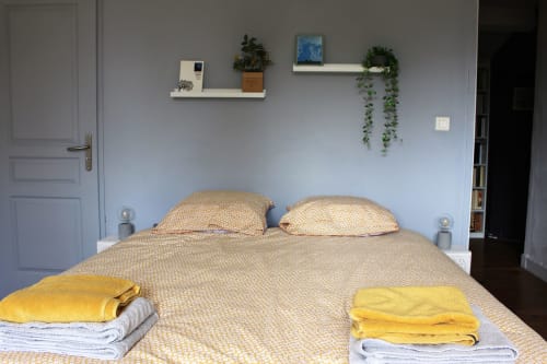 Chambre cosy du gîte Les Petits Toits à Vérac, avec linge de lit crème, serviettes jaunes et étagères donnant sur le jardin