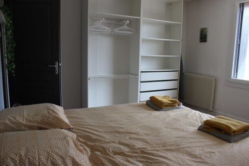 Chambre spacieuse du gîte Les Petits Toits avec placard intégré, serviettes dorées soigneusement arrangées et fenêtres avec vue sur le jardin