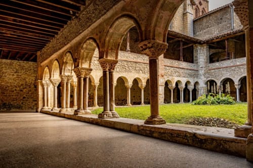 Cloître médiéval aux arcades en pierre, colonnes de calcaire et cour herbue à Ferrières-sur-Ariège