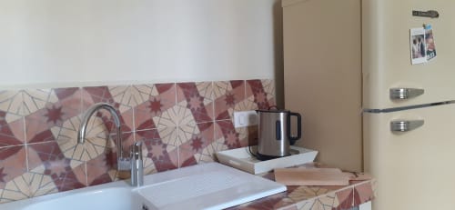 Cottage kitchen area in Arles featuring decorative red tile backsplash, stainless steel kettle, white sink, and chrome faucet