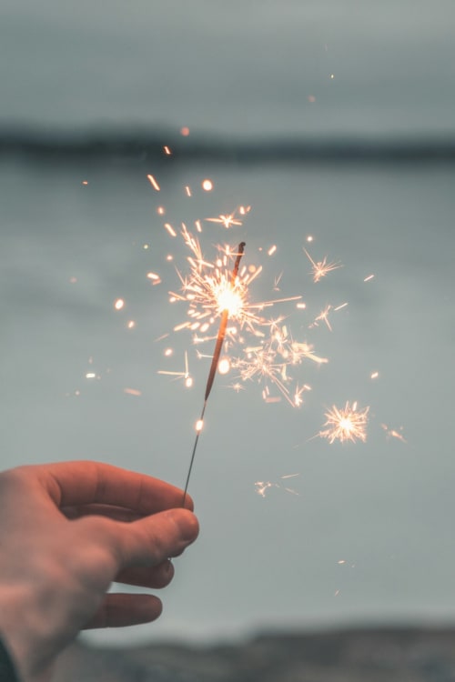 Hand holding a lit sparkler against a twilight sky near Ô Château hotel in Hayange, France