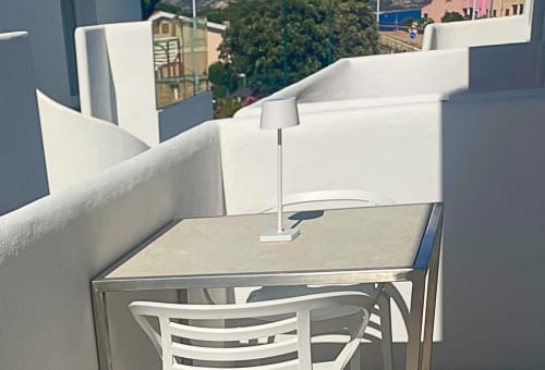 Moderna terrazza sul tetto del Like at Home Palau con arredamento bianco, lampada e vista sulla campagna di Palau oltre i muri bianchi